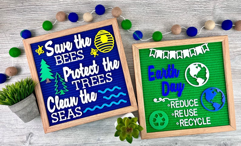 May include: Two square felt letter boards with light wood frames. The blue board displays white text reading Save the Bees, Protect the Trees, Clean the Seas with bee, hive, tree, and wave icons. The green board displays Earth Day and recycling text.