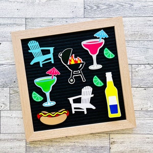 May include: A square felt letter board with a light wood frame featuring various summer-themed icons including a light blue Adirondack chair, a black charcoal grill with flames, a pink cocktail with a blue umbrella, a green cocktail with a pink umbrella, a white Adirondack chair, a yellow beer bottle, a hot dog, and lime wedges.