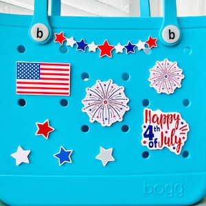 May include: A bright turquoise tote bag decorated with patriotic-themed stickers. The bag features an American flag, star-shaped stickers, and fireworks designs. The text "Happy 4th of July" is also visible.