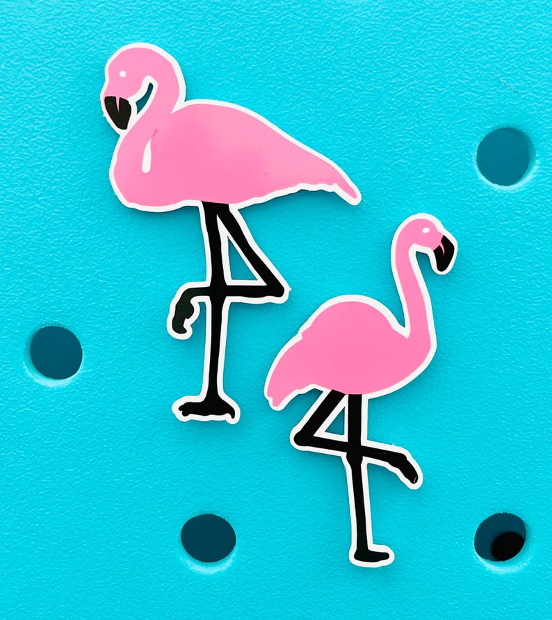 K&ouml;nnte beinhalten: Zwei rosa Flamingo-Aufkleber mit schwarzen Beinen und Schn&auml;beln werden vor einem hellt&uuml;rkisen Hintergrund gezeigt. Die Flamingos sind in verschiedenen Posen, einer steht und der andere hat das Bein gehoben. Die Aufkleber haben eine wei&szlig;e Umrandung.