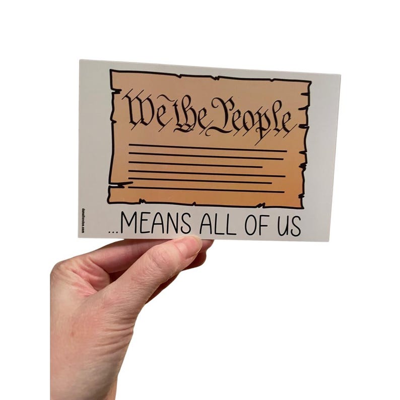 Puede incluir: Una pegatina rectangular con el texto "We the People" en una fuente estilizada, encima de las palabras "...MEANS ALL OF US". El fondo es de color pergamino, con bordes y texto negros.