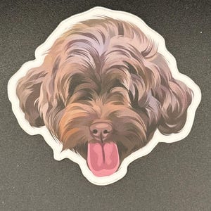 May include: A sticker featuring a detailed illustration of a dog's face. The dog has brown fur, a pink nose, and a pink tongue sticking out. The sticker has a white border and is set against a dark background.