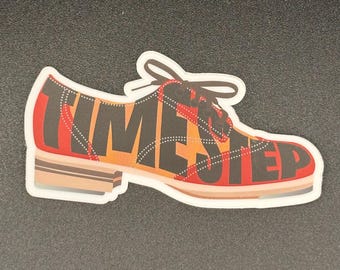 May include: A sticker in the shape of a shoe with the words "TIME STEP" in black letters. The shoe has a plaid pattern in red, orange, and black. The laces are black, and the sole is brown.