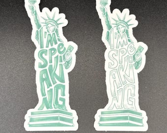 Pode incluir: Dois adesivos com a Estátua da Liberdade em contorno verde. O texto "I'M SPEAKING" está integrado no design da estátua. Os adesivos estão em um fundo escuro.