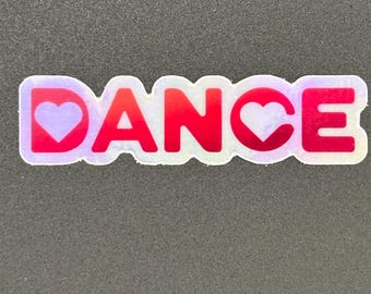 May include: A sticker with the word "DANCE" in red, outlined in white, with a heart replacing the "O" in the word. The background is a dark gray color.