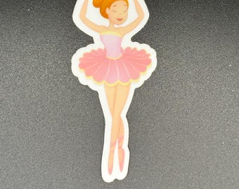 May include: A sticker of a ballerina in a pink tutu and ballet shoes. The ballerina has her arms raised above her head. Her hair is styled in a bun. The sticker has a white border.