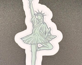 May include: A sticker featuring a stylized illustration of the Statue of Liberty in a ballet pose. The figure is depicted in a light green color, holding a torch and a book, with a tutu-like skirt and pointe shoes.