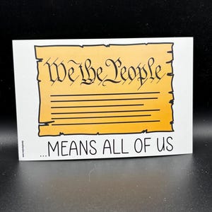 May include: A rectangular sticker with the text "We the People" in a decorative font, above the words "...MEANS ALL OF US." The background is yellow with horizontal lines, and the border is black.
