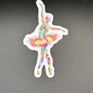 May include: A sticker of a ballerina in a tutu, with arms raised. The dancer is depicted in a watercolor style, with a vibrant mix of colors including red, blue, green, and yellow. The sticker has a white border.