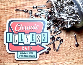 May include: A sticker with a red and light blue retro sign design featuring the text Chronic Illness Cafe and the phrase Plenty of pots, never enough spoons, accompanied by a pile of small silver-colored metal spoon charms.