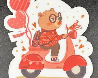 May include: A sticker featuring a cartoon bear riding a red scooter, holding heart-shaped balloons. The bear wears glasses, a sweater, and a backpack. A small bird carries a letter. The text "for you" is on a tag.