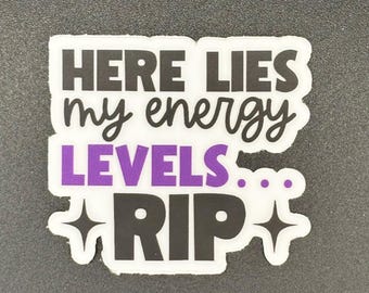 May include: A white sticker with black text that reads "HERE LIES my energy LEVELS... RIP". The word "LEVELS" is in purple. The sticker has a starburst design on the bottom.