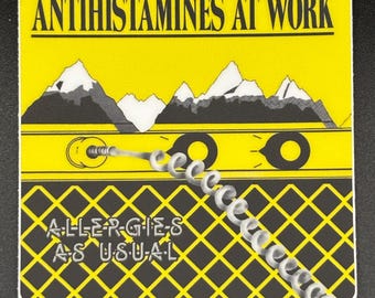 May include: A yellow sticker with black text that reads "ANTIHISTAMINES AT WORK" above a mountain range graphic. Below the mountains is a graphic of a cassette tape with a coiled cord. The bottom of the sticker reads "ALLERGIES AS USUAL".