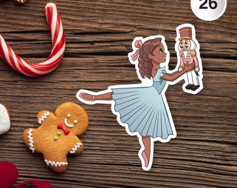 May include: A sticker of a ballerina in a light blue dress holding a nutcracker. The sticker is on a wooden surface with a gingerbread man, candy cane, and other holiday treats.