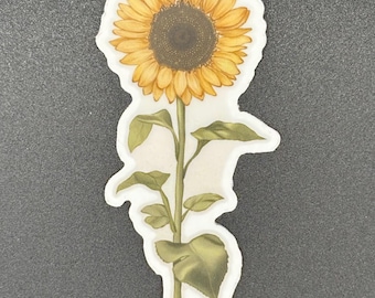 May include: A die-cut sticker featuring a watercolor illustration of a sunflower. The sunflower has yellow petals and a dark brown center. The stem and leaves are green, and the sticker has a white border.