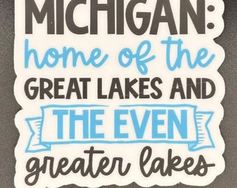 May include: A white die-cut sticker featuring the black text MICHIGAN: home of the, the blue text GREAT LAKES AND, the blue text THE EVEN inside a blue banner, and the black text greater lakes at the bottom in a script font style.