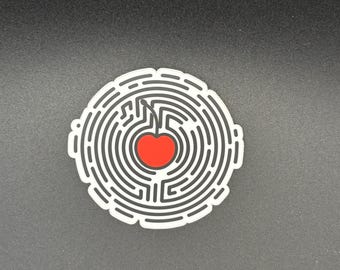 May include: A white sticker with a black maze design surrounding a red cherry. The cherry has a stem and is in the center of the maze. The sticker is on a black surface.