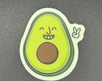 May include: A sticker featuring a smiling avocado with a brown pit and a peace sign. The avocado is green with a lighter green border and a white outline. The sticker has a cartoon style.