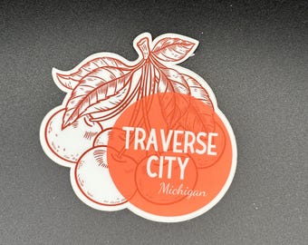 May include: A sticker featuring a cluster of cherries with leaves. The design includes a red-orange circle with the words "TRAVERSE CITY Michigan" in white. The cherries and leaves are outlined in brown.