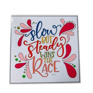 May include: A colorful square sign with a white background and the text "slow but steady wins the race" in a rainbow font. The text is surrounded by pink, red, and green teardrop shapes.