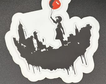 May include: A sticker featuring a silhouette of a child holding a red cherry balloon above a cityscape. The cityscape is black with white outlines and dripping paint effect. The cherry balloon has a red and black design.