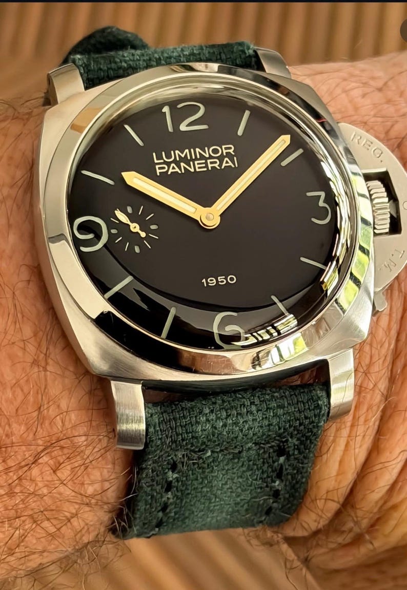 May include: A close-up of a luxury wristwatch with a black face, gold hands, and a silver case. The watch has the text "LUMINOR PANERAI 1950" on the face and a dark green fabric band.