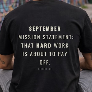 Può includere: Una t-shirt nera a maniche corte con testo bianco sul retro che recita: SEPTEMBER MISSION STATEMENT: THAT HARD WORK IS ABOUT TO PAY OFF. Il capo è indossato con jeans grigi e un berretto, abbinato a uno skateboard.