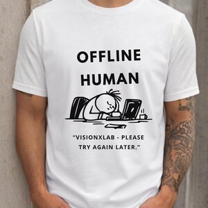 Puede incluir: Una camiseta blanca de manga corta con el texto negro "OFFLINE HUMAN" sobre un gráfico de una figura de palo durmiendo ante un portátil. Debajo del gráfico, el texto dice "VISIONXLAB - PLEASE TRY AGAIN LATER." La camiseta tiene cuello redondo.