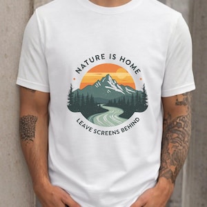 May include: White t-shirt with a nature-themed graphic. The design includes a mountain range, a winding road, and the text "NATURE IS HOME LEAVE SCREENS BEHIND" in a circular arrangement. The graphic uses shades of orange, green, and blue.