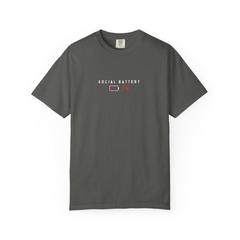 May include: Dark gray t-shirt with the text "SOCIAL BATTERY" above a red battery icon showing 1% charge. The shirt has short sleeves and a crew neck.