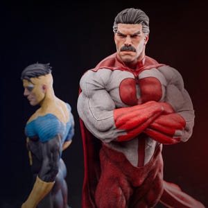 Puede incluir: Dos figuras de acción de superhéroes. Una figura viste un traje rojo, blanco y gris con capa roja y brazos cruzados. La otra figura viste un traje azul y amarillo. Ambas figuras tienen rasgos faciales detallados y cuerpos musculosos, sobre un fondo oscuro.