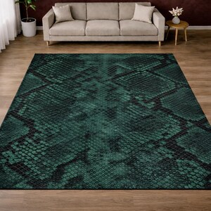 May include: A rectangular rug featuring a snakeskin design in shades of green and black. The rug is positioned on a wooden floor, with a beige sofa and side table visible in the background. The rug's pattern mimics reptile scales.