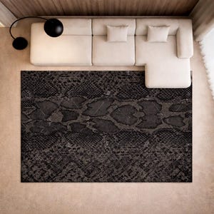 Puede incluir: Una alfombra gris oscuro con un patrón de piel de serpiente está centrada en una habitación. Un sofá seccional beige con dos cojines cuadrados se encuentra encima de la alfombra. Una lámpara negra moderna está colocada a la izquierda del sofá.