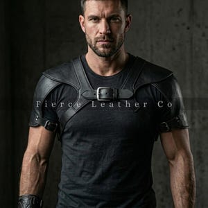 Może przedstawiać: Czarna skórzana zbroja na ramię z regulowanymi paskami i klamrami. Zbroja jest noszona na czarnym t-shircie. Tekst "Fierce Leather Co" jest widoczny na zbroi. Obraz jest na ciemnym tle.