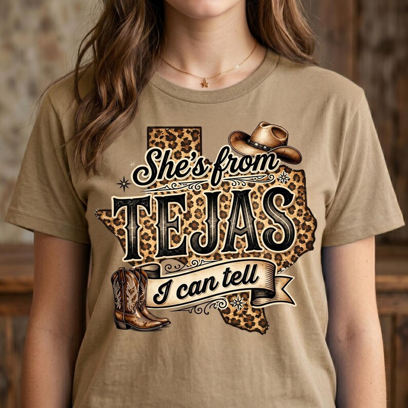 May include: A tan t-shirt featuring a graphic design with the text "She's from TEJAS I can tell." The design includes a cowboy hat, cowboy boots, and a leopard print Texas outline.