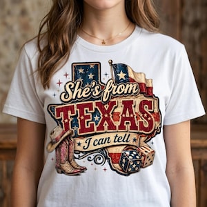 May include: White t-shirt featuring a graphic design with the text "She's from TEXAS I can tell". The design includes a Texas outline, a flag, cowboy boots, a hat, and dice.