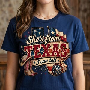 May include: Navy blue t-shirt with a graphic that reads "She's from TEXAS I can tell." The design includes a Texas flag, cowboy boots, a cowboy hat, and dice. The graphic is in red, white, and blue.