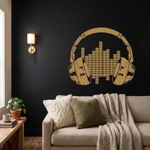 May include: A gold-coloured wall art piece featuring headphones with an equaliser graphic. The headphones have detailed earcups and a connecting band. The art is mounted on a black wall, creating a striking contrast.