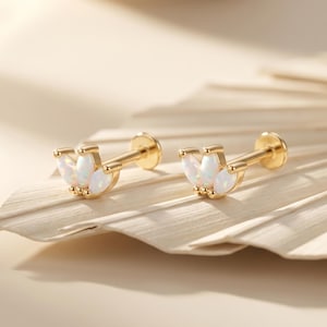 Op de afbeelding: Een paar gouden oorknopjes met een cluster van drie marquise-geslepen witte opalen in een waaiervorm. Elke oorknop heeft een rechte stift en een platte ronde achterkant, met een gepolijste metalen afwerking en iriserende stenen.
