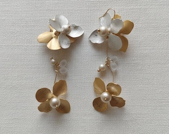 May include: A pair of floral earrings with a gold and silver finish. Each earring features a cluster of flower-shaped petals with a pearl center and dangling pearl accents. The earrings are designed for pierced ears.