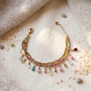 May include: A multi-strand gold chain bracelet featuring small faceted green and pink beads, accented with dangling polished gemstone drops in various colours including blue, pink, yellow, and green, finished with a gold lobster claw clasp.