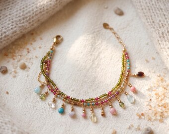 May include: A multi-strand gold chain bracelet featuring small faceted green and pink beads, accented with dangling polished gemstone drops in various colors including blue, pink, yellow, and green, finished with a gold lobster claw clasp.