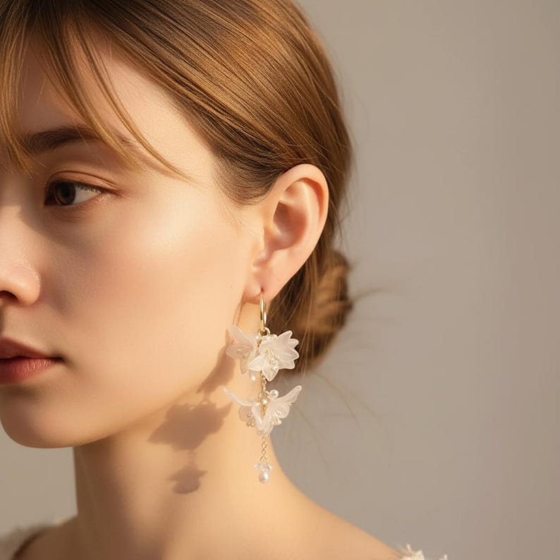 May include: Elegant gold hoop earrings with delicate white flower and butterfly charms. The earrings feature small pearl accents and dangle gracefully. The design is feminine and suitable for special occasions or everyday wear.