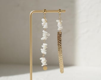 May include: A pair of asymmetrical earrings. One earring features a strand of white, irregular-shaped stones, while the other has a long, textured gold bar. Both earrings are suspended from gold-colored posts.