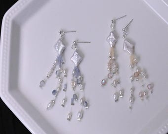 May include: Two pairs of dangle earrings featuring a central diamond-shaped white pearl at the top. One pair is accented with blue and white beads, while the other pair features soft pink and white beads, all hanging on thin silver-toned posts.