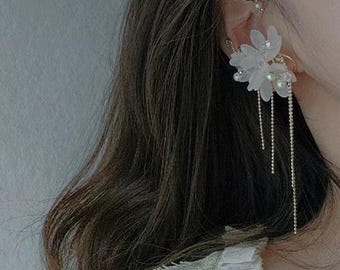 May include: A floral ear cuff and earring set. The ear cuff features a delicate design with small pearls and a gold-tone finish. The earring has a cluster of white flowers with dangling gold chains. The jewelry is worn on the ear.