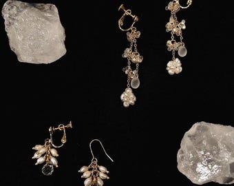 May include: Two pairs of gold-toned earrings featuring clusters of small white freshwater pearls and clear teardrop-shaped beads. One pair consists of long drop clip-on earrings, while the other pair includes one clip-on and one hook earring.