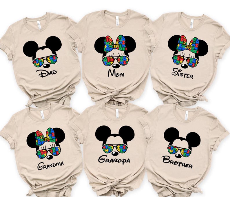 Beige family matching autism awareness shirts, featuring Mickeystyle ears, sunglasses or bows with colorful autism puzzle pieces, labeled Dad, Mom, Sister, Brother, Grandma, and Grandpa.