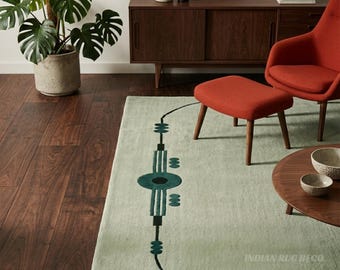 May include: A rectangular area rug in a light sage green color featuring a dark teal and black geometric pattern running vertically along the center. The design consists of a central circle, parallel lines, and small oval shapes in a linear arrangement.