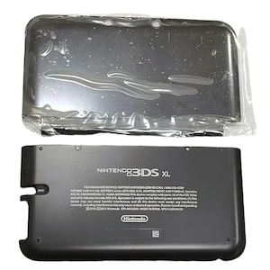 May include: A black Nintendo 3DS XL console, with the top half in a clear plastic wrap. The bottom half of the console is visible, displaying the Nintendo logo and product information. The console is a handheld gaming device.